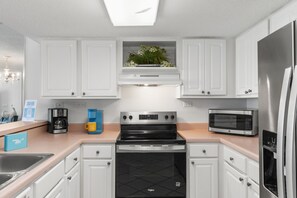 A modern kitchen with white cabinets, a stainless steel refrigerator, a microwave, and a coffee maker.
