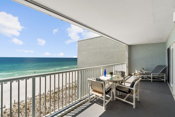 A balcony with a view of the beach and ocean, furnished with a table and chairs, and a small potted plant.