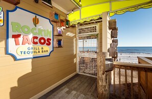 Un restaurante junto a la playa llamado 'Rockin' Tacos', con un letrero, una terraza de madera y vistas al océano.