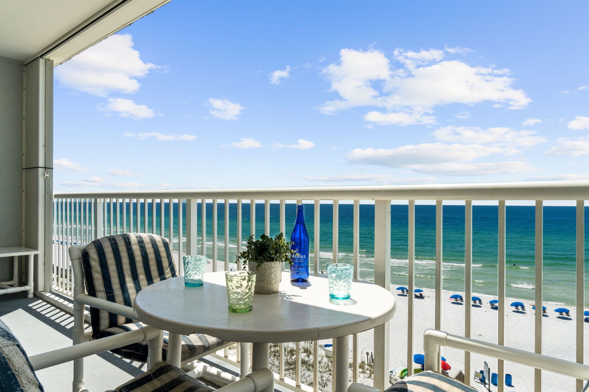 Ein Balkon mit Blick auf den Strand, ein Tisch mit einem Topfpflanzen und eine blaue Flasche.