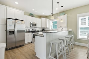 A modern kitchen with white cabinetry, stainless steel appliances, a central island with bar stools, and pendant lighting.