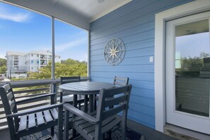 A covered patio with a table and chairs, a compass wall decoration, and a view of buildings and trees.