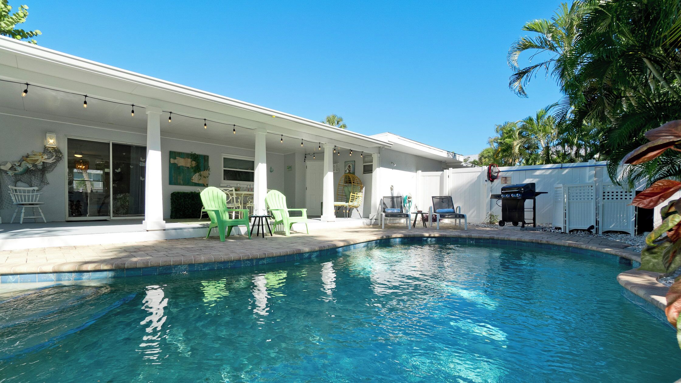 A pool area with a covered patio, outdoor seating, and a barbecue grill.