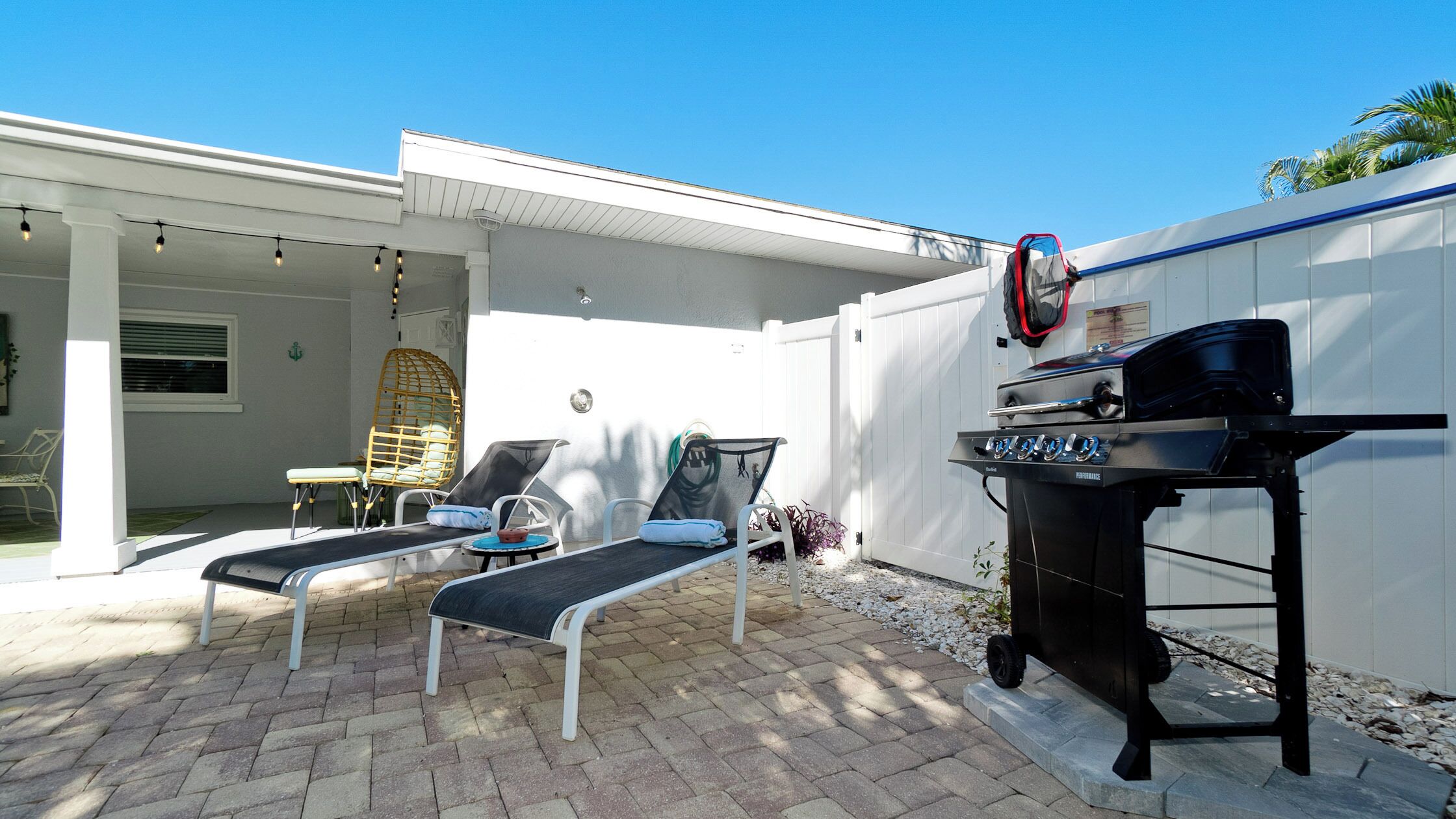 Un patio con dos sillones de descanso, una parrilla y una zona de estar cubierta.