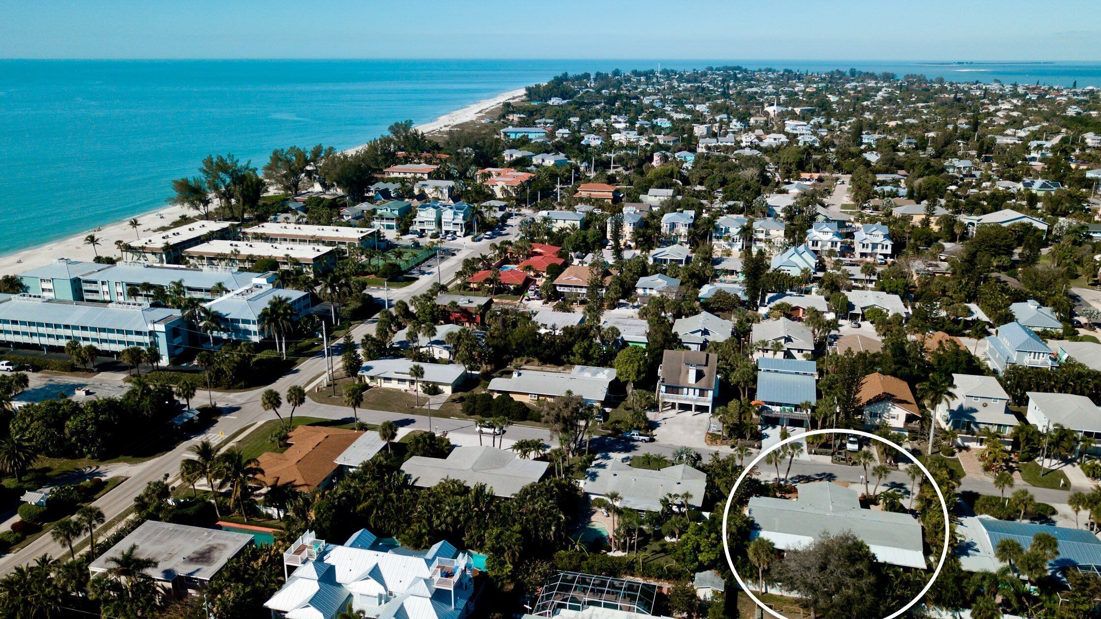 An aerial view of a coastal residential area with houses, a beach, and a large hotel complex.