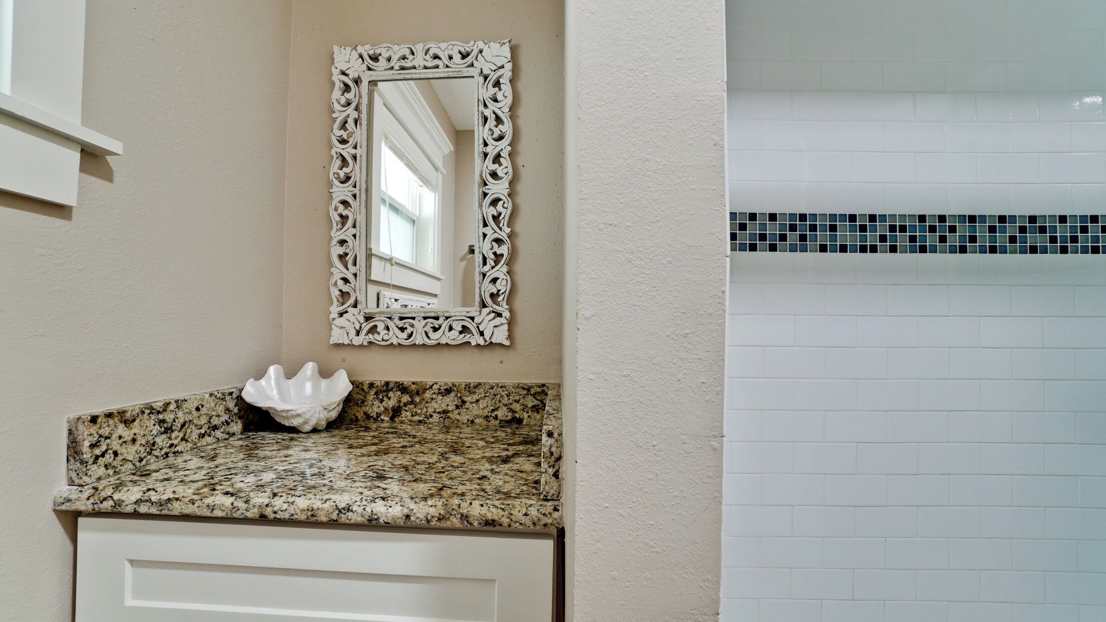 Un baño con encimera de granito, un espejo decorativo y un salpicadero de azulejos.
