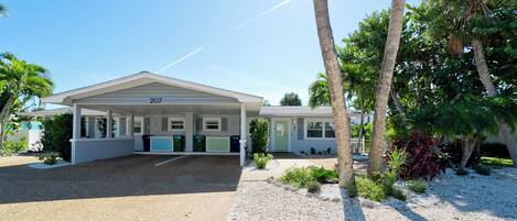 A single-story house with a covered porch, numbered 207, surrounded by palm trees and a gravel driveway.