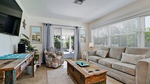 Una sala de estar con sofá, mesa de centro, televisor y ventana con persianas.