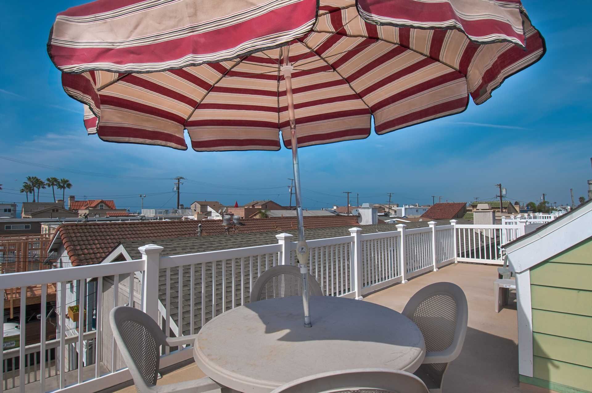 Un balcon avec une table et des chaises, un parasol à rayures et une vue sur des immeubles et des palmiers.