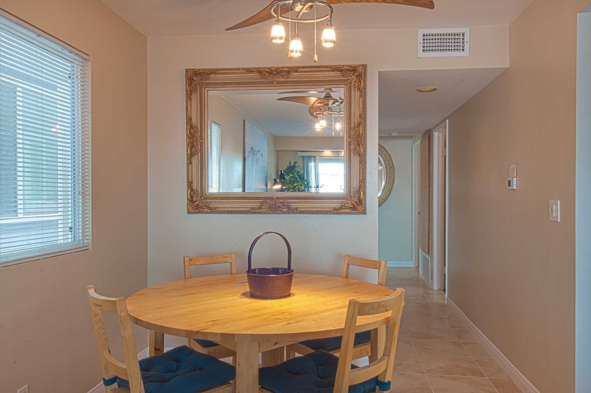 A dining area with a round wooden table, four chairs, a large mirror, and a ceiling fan.