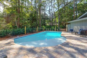 Une piscine dotée d’une terrasse carrelée, entourée d’une clôture et d’arbres.
