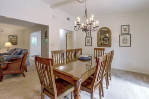 Un coin repas avec une table à plateau de verre entourée de chaises en bois, un lustre et des œuvres d’art encadrées accrochées aux murs.