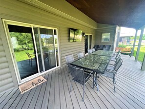 A covered outdoor dining area with a glass table and chairs, sliding glass doors, and a wooden deck. - Big Sky Lodge @ Spring Brook Resort (Wisconsin Dells)