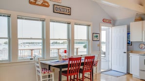 A dining area with a table and chairs, large windows with a view of boats, and a sign that reads "OYSTERS". - 'Heron Cottage' on Casco Bay w/ Deck & Boat Dock! (Freeport)