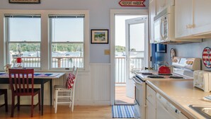 A kitchen with a view of the harbor, a dining area with a table and chairs, and a sign indicating Freeport Harbor. - 'Heron Cottage' on Casco Bay w/ Deck & Boat Dock! (Freeport)