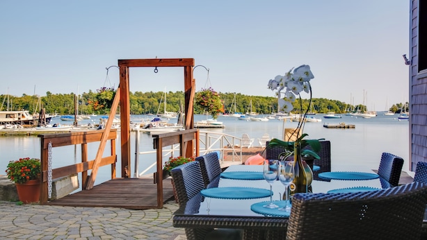 A wooden deck with wicker furniture overlooking a marina. - 'Heron Cottage' on Casco Bay w/ Deck & Boat Dock! (Freeport)