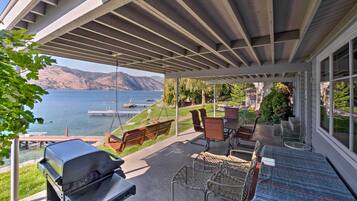 A covered patio with a grill, seating, and a view of the lake.