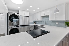 A modern kitchen with stainless steel appliances, white cabinetry, a built-in oven, and a large island. - Direct Oceanfront Bliss: Ground-Floor Condo with Heated Pool & Private Beach Access 🌊☀️ (Satellite Beach)