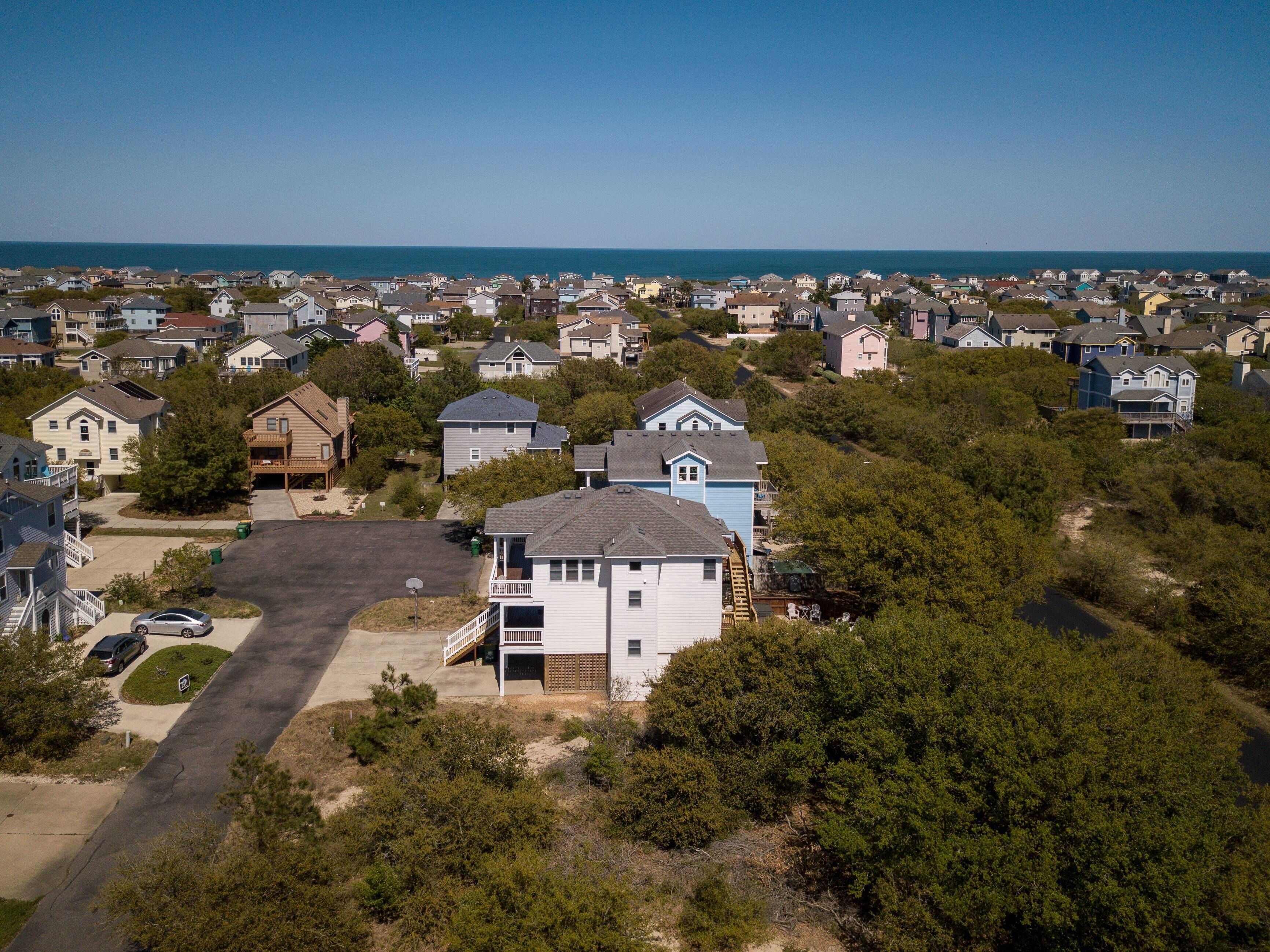 An aerial view of a residential area with houses, a clear sky, and a body of water in the background.