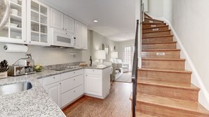 A kitchen with white cabinets, a granite countertop, and a wooden staircase.