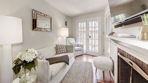 A living room with a white sofa, a side table with a vase of flowers, a lamp, and a fireplace.