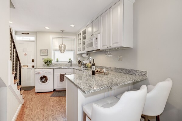 A modern kitchen with white cabinetry, a granite countertop, and a built-in washing machine.