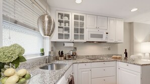 A modern kitchen with white cabinetry, granite countertops, and a stainless steel sink.