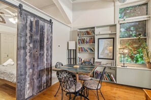 A room with a wooden door, a dining table with chairs, a bookshelf, a map on the wall, and a window with a view of greenery. - Historic Loft w/ Private Deck, 2 Blocks to Dtwn (Saugatuck)