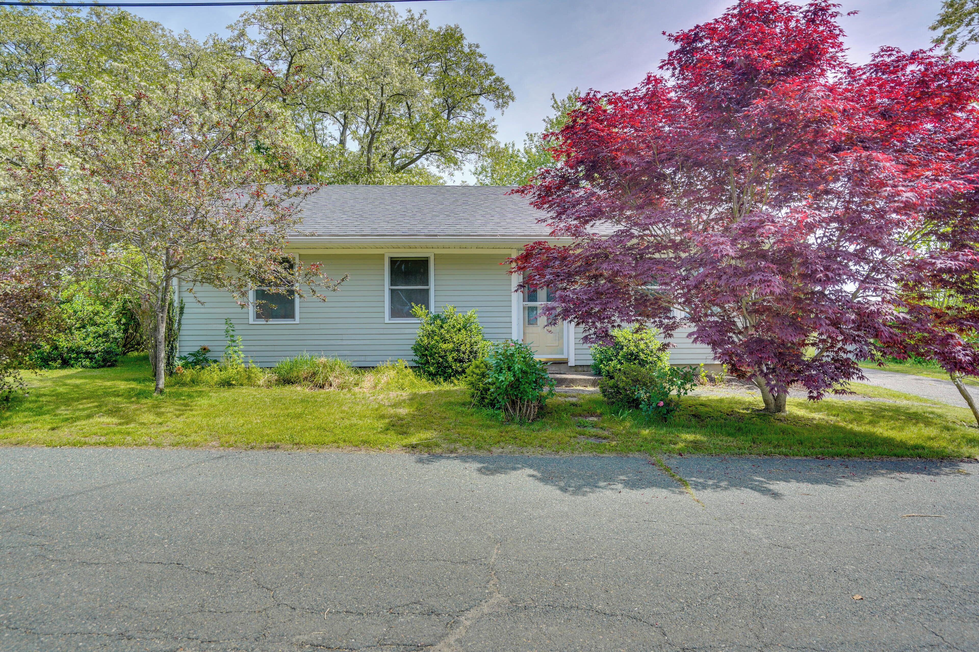 A single-story house with a front yard, a driveway, and a tree with red leaves.