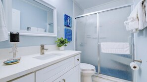 A bathroom with a white vanity, a glass shower enclosure, and a blue seahorse artwork on the wall.