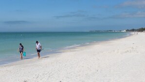 A beach with two people walking along the shore, carrying beach gear.