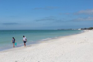 A beach with two people walking along the shore, carrying beach gear.