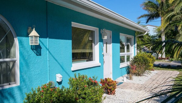 A turquoise house with white trim, a white door, and a small porch area with plants.