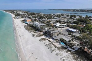 An aerial view of a coastal town with a beach, buildings, and a pier.
