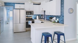 A modern kitchen with white cabinets, a blue backsplash, and a central island with bar stools.