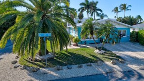 A blue house with a sign reading "12 St. N." surrounded by palm trees and a gravel driveway.