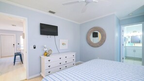 A bedroom with a bed, dresser, TV, and a round mirror on the wall.
