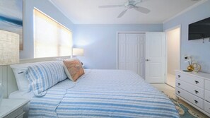 A bedroom with a bed, a nightstand, a dresser, a ceiling fan, and a TV on the wall. - Coastal Family Retreat with Heated Pool | Walk to Beach | Dog Friendly (Bradenton Beach)