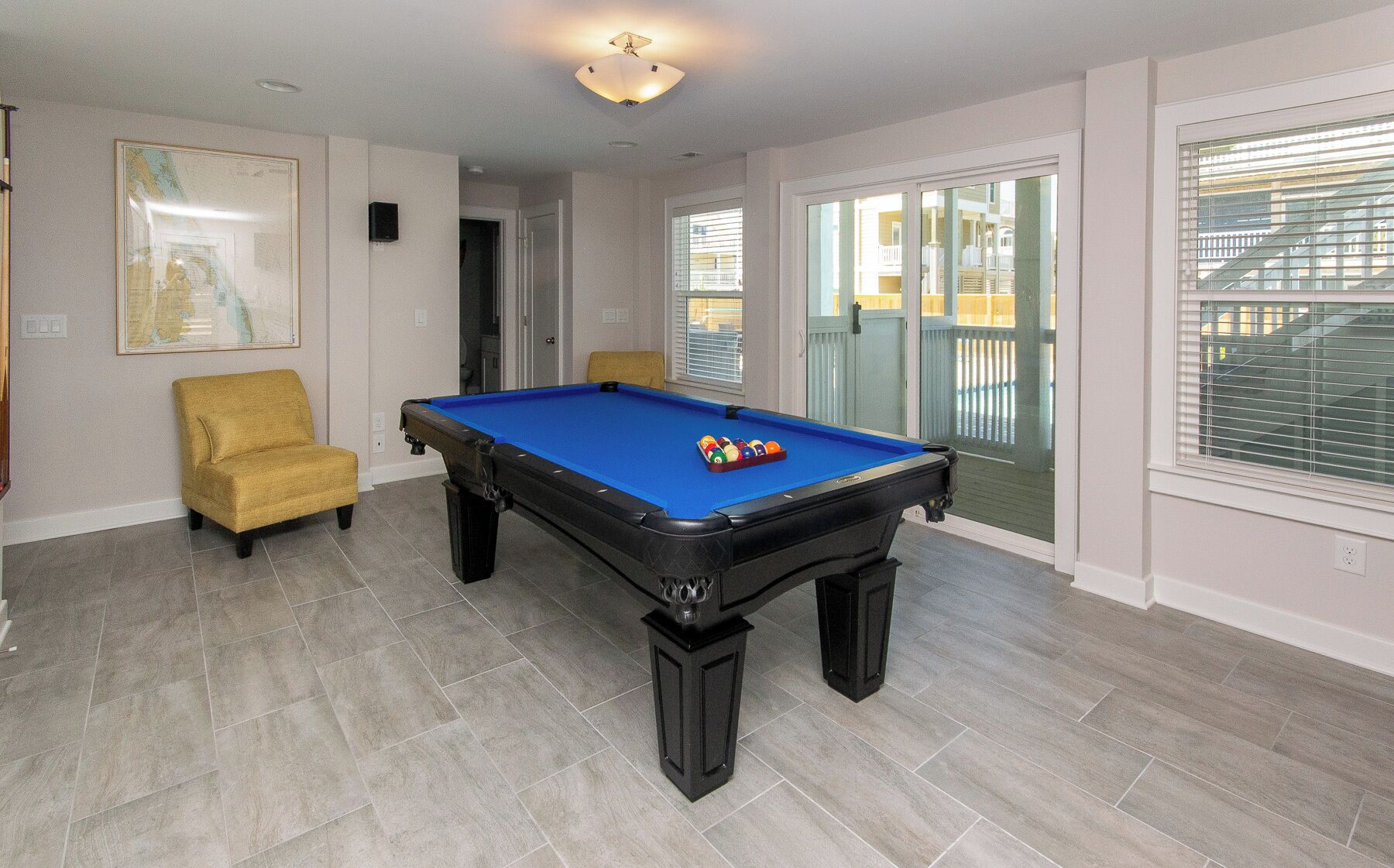 A pool table in a room with a yellow armchair, a framed map on the wall, and a balcony with a view.