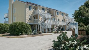A multi-story hotel with a central staircase, a sign reading "Pelican Courts," and a cactus plant in the foreground.