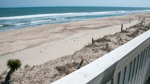 A beach with a wooden railing, sandy shore, and sparse vegetation.