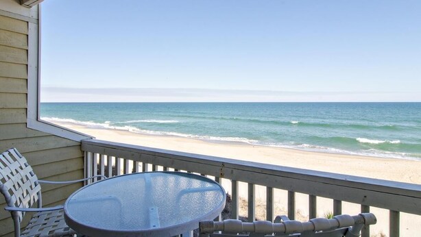 A balcony with a table and chairs overlooking a beach.