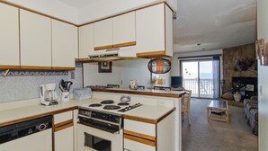 A compact kitchen with a stove, oven, and dishwasher. There is a dining area with a table and chairs, and a living room with a sofa and a fireplace.