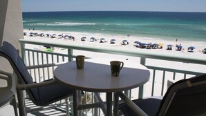 A balcony with a view of a beach. There are two chairs and a small table with two cups on it. - PI 412: Island Oasis - Enjoy a splashing good time at this beachfront condo! (Fort Walton Beach)