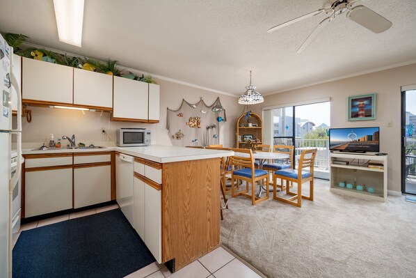 A modern kitchen with white cabinets, a wooden island, and a dining area with blue chairs. - Located close to the ocean, shops, dining and water activities. Ocean view from balcony. (Ocean city)