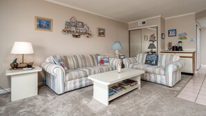 Una sala de estar con sofás a rayas, una mesa de centro blanca y una mesita auxiliar con una lámpara.