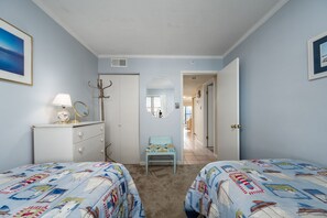 Une chambre avec deux lits, une commode, un miroir et une porte donnant sur une autre pièce.