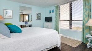 Un dormitorio con cama, ventilador de techo, televisión, cómoda y ventana con persianas.