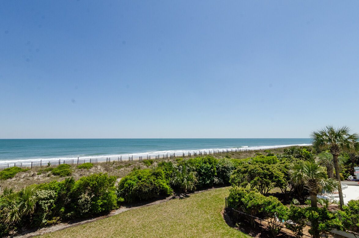 Vista costeira com praia, cerca e vegetação exuberante.