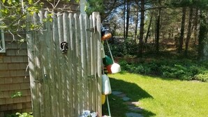 Ett trähus med en liten dörr, en trädgårdsgång och diverse föremål som hänger på dörren, bland annat en grön hink, en vit hink och en rosa väska.